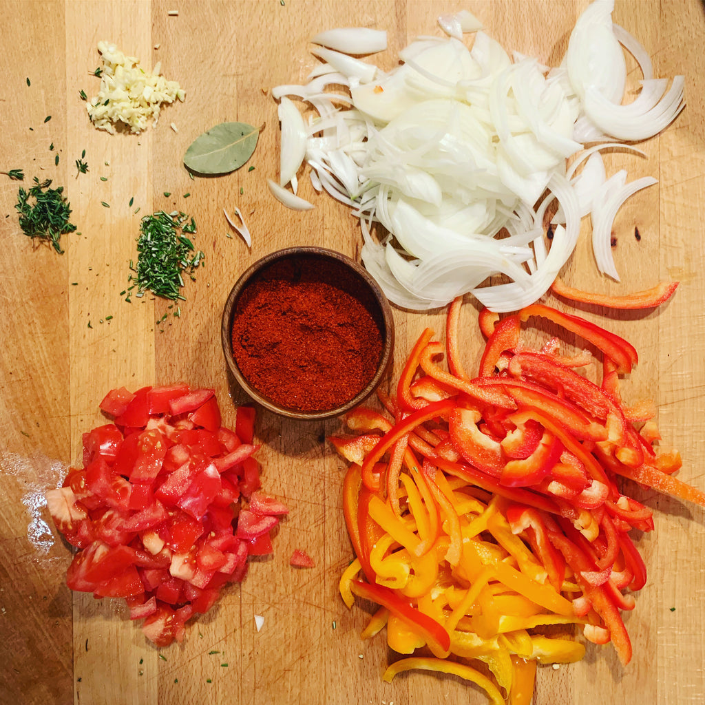 cutting board wiht sliced onion pepper tomato herbs and espelette chile